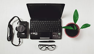 black laptop beside green leaved potted plant and black film camera and twist pen and black frame eyeglasses