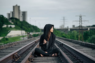 selective focus photography of woman in black hoodie and pants sitting on train track