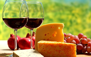 two wine on wine glasses; sliced cheese; grapes and pomegranates