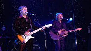 two men wearing casual attire singing and playing guitar