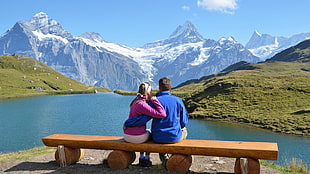 couple sitting in front of body of water and snow mountain during daytime
