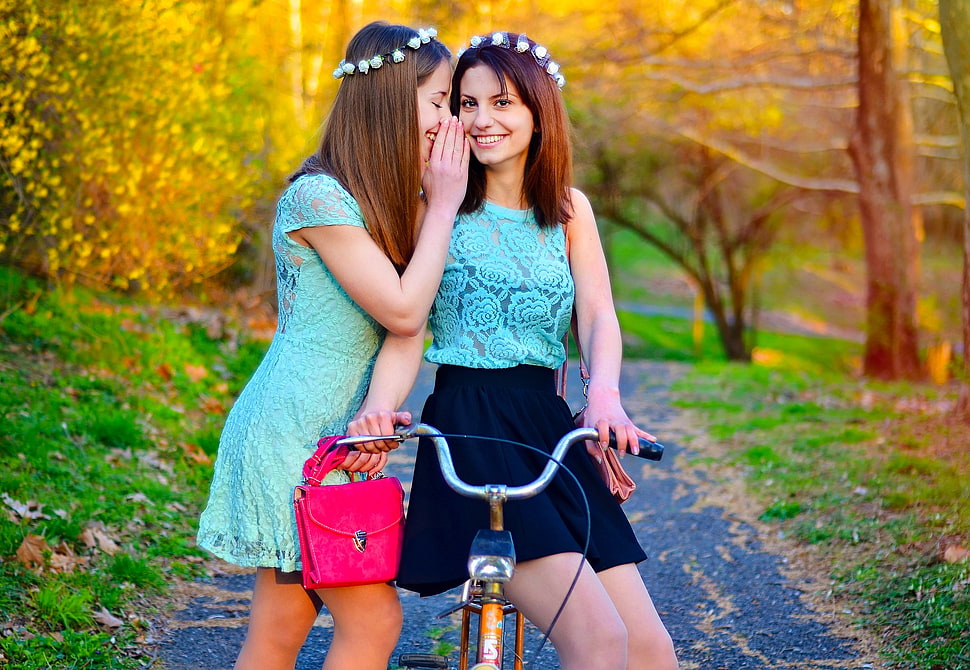 woman wearing teal cap sleeve whispering woman on riding bicycle HD wallpaper