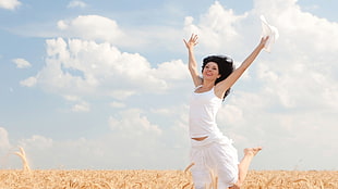 woman wearing white tank top jump on brown grass field during daytime