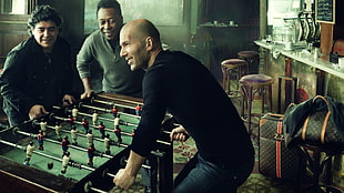 man wearing black crew-neck long-sleeved shirt playing foosball table