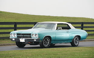 classic teal muscle car on concrete road near black wooden fence