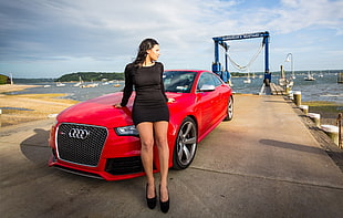 photo of woman leaning on red Audi coupe during daytime