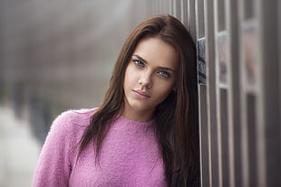 depth of field photography of woman wearing pink top leaning on wall