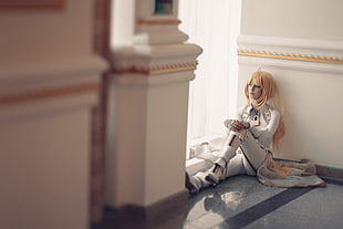 blonde haired woman wearing white leather top and pants sitting beside window pane
