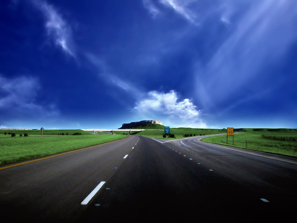 gray road pavement in between green fields towards green mountain HD wallpaper
