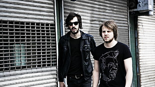 high saturated photography of two men wearing black cloths standing near roller shutter during daytime