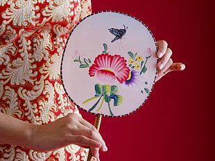 person holding white, green and red floral hand fan