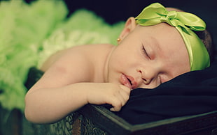baby wearing green headband sleeping on black textile