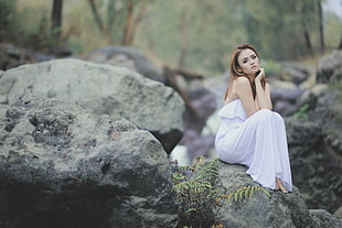 woman wearing white dress sitting on rock formation