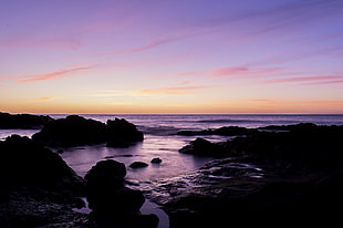 silhouette of rock on the seashore during sunset