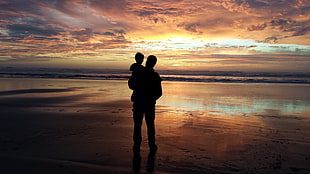 silhouette of man and boy on seashore under cloudy sky during golden hour HD wallpaper