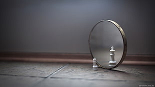 shallow focus photography of pawn chess piece in front of round mirror with reflection a king
