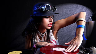 female DJ playing turntable wearing black cap and white sleeveless top