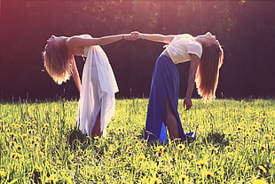 two woman holding hands standing on green grass field during daytime