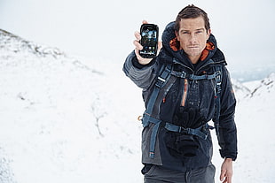man holding smartphone behind snow