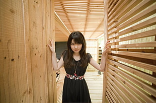 woman wearing black sleeveless dress holding brown wooden door