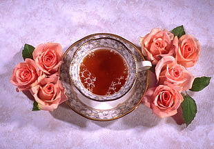 tea in ceramic teacup with saucer near pink Rose flowers acceent