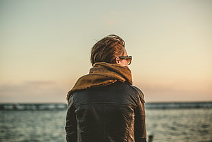 person wearing brown scarf and leather jacket facing body of water