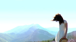 woman in white floral short-sleeved dress next to mountain range during daytime