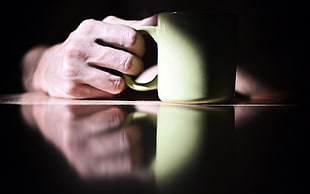person holding yellow ceramic mug on table