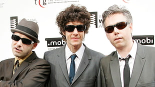 man in gray suit jacket in between two men wearing black sunglasses