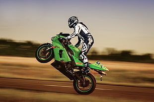 time lapse photography of person wearing white and black racing suit riding green Kawasaki Ninja doing high speed wheelie during daytime