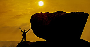 silhouette photo of man standing near huge rock during golden hour HD wallpaper