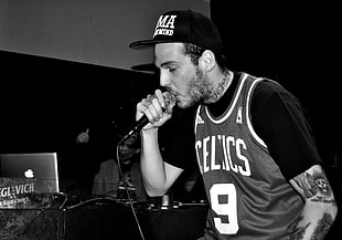 photo of man wearing black cap, t-shirt, and Boston Celtics jersey top while holding microphone