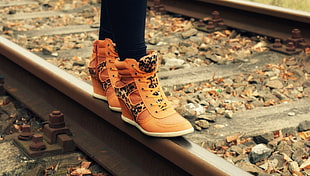 person in pair of orange high-top sneakers walking on railroad track HD wallpaper