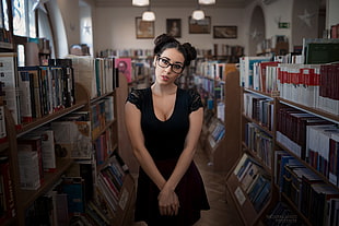 woman wearing black cap-sleeved top standing between brown book shelves