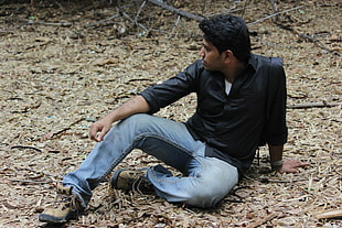 man in black dress shirt and blue jeans sitting on ground