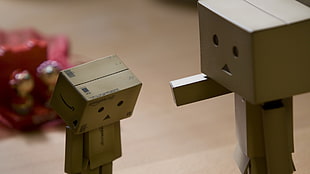 depth of field photo of two DIY box human figures on top of brown wooden table