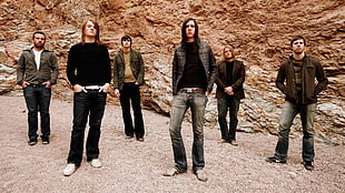 six men standing wearing denim pants with and brown rocky hill background