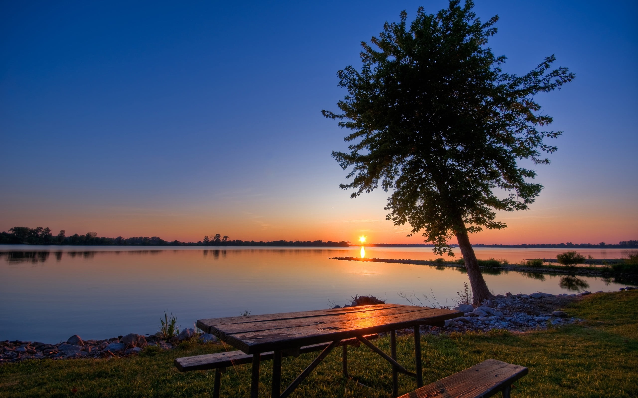 photo of rectangular brown picnic table near lake during sunset