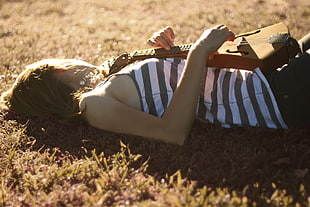woman in striped tank top lying on grass field at daytime
