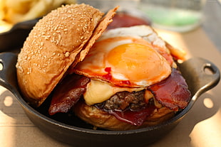 selective focus photography of hamburger with egg and bacon in skillet