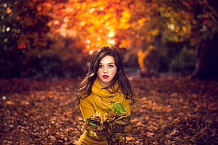 woman wearing yellow sweatshirt in forest surrounded by dried leaves