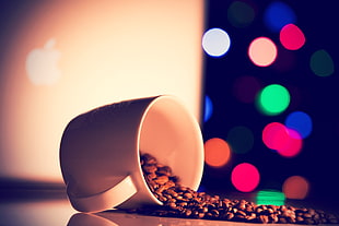 white ceramic cup with brown coffee beans on brown wooden table with bokeh lights in the background