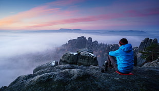person wearing blue jacket sitting on rocky mountain during daytime HD wallpaper