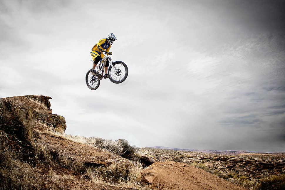 man in yellow sports shirt riding bicycle jumping on brown mountain cliff during daytime HD wallpaper