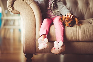 child sitting on sofa beside brown dog