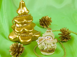 photo of baby figurine and three gold-colored pine cones on green textile