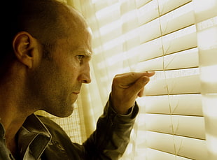 man looking through white window blinds