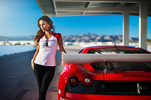 woman in white polo shirt standing beside red sports car