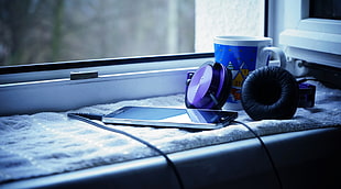 black and purple headphones beside ceramic mug near window pane