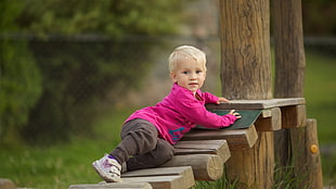 child in pink sweater and black pants laying on wood during daytime